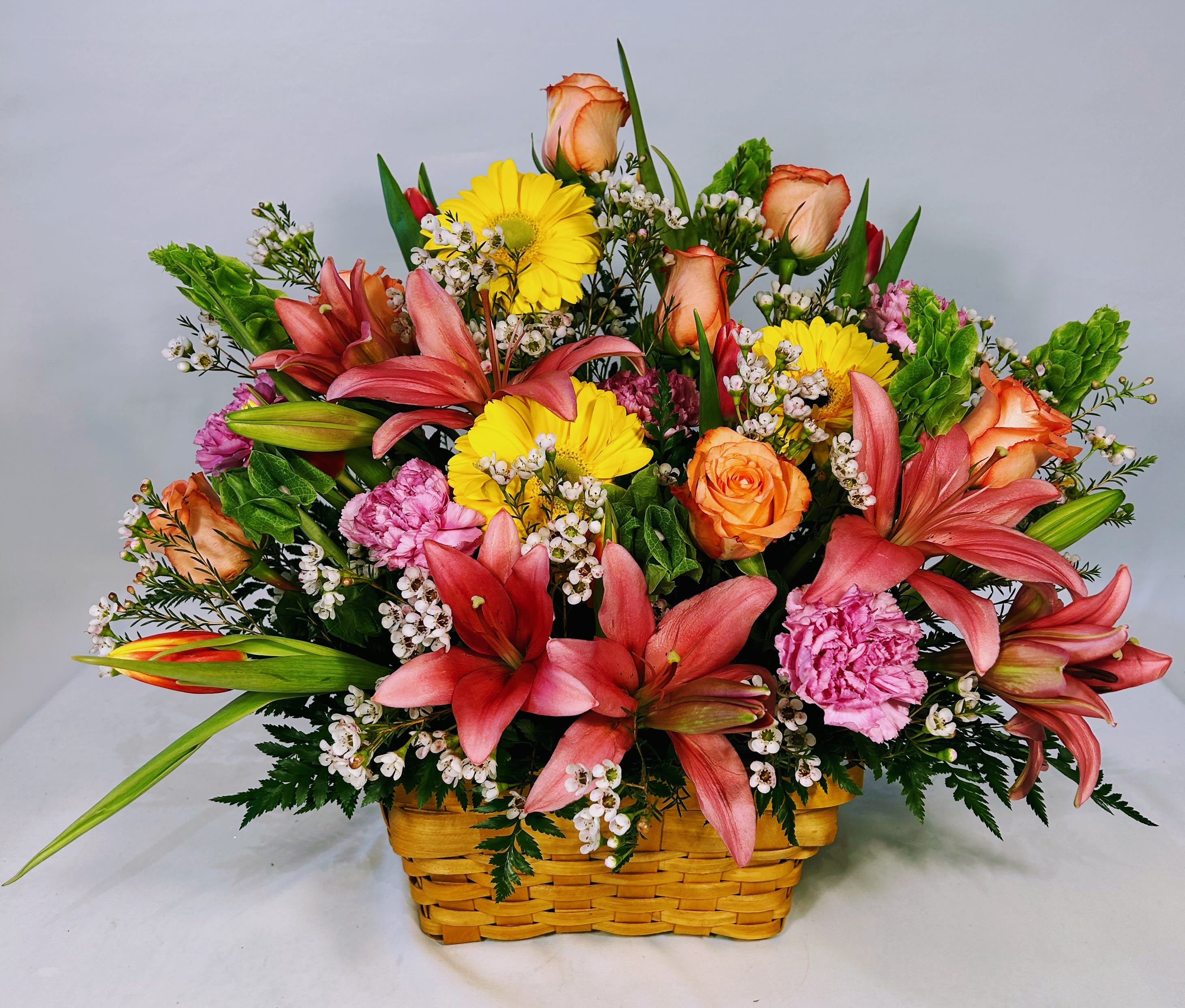 Colorful basket arrangement with pink lilies, yellow gerberas, orange roses, and pink carnations.