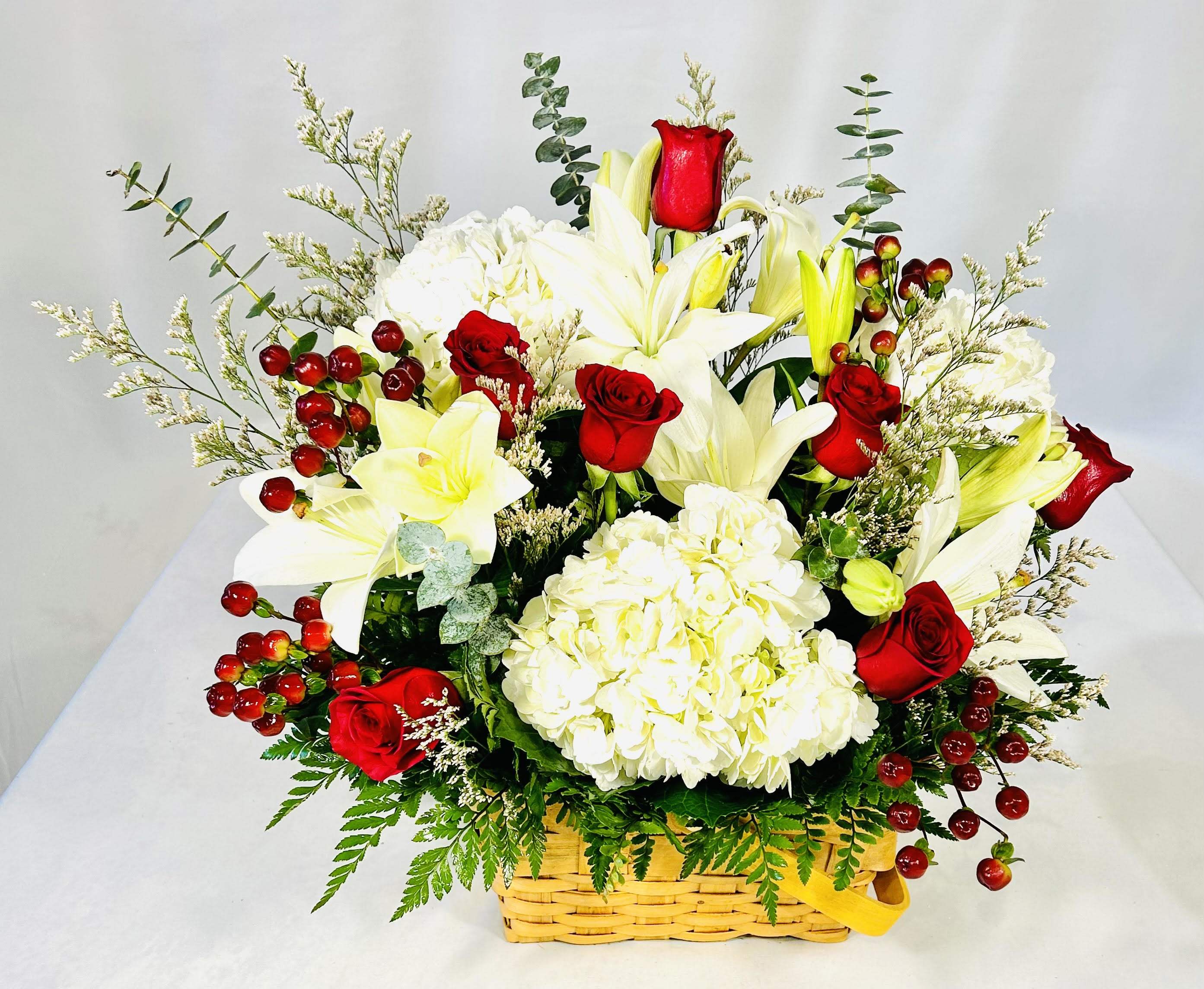 Basket arrangement of white lilies, red roses, and white hydrangea