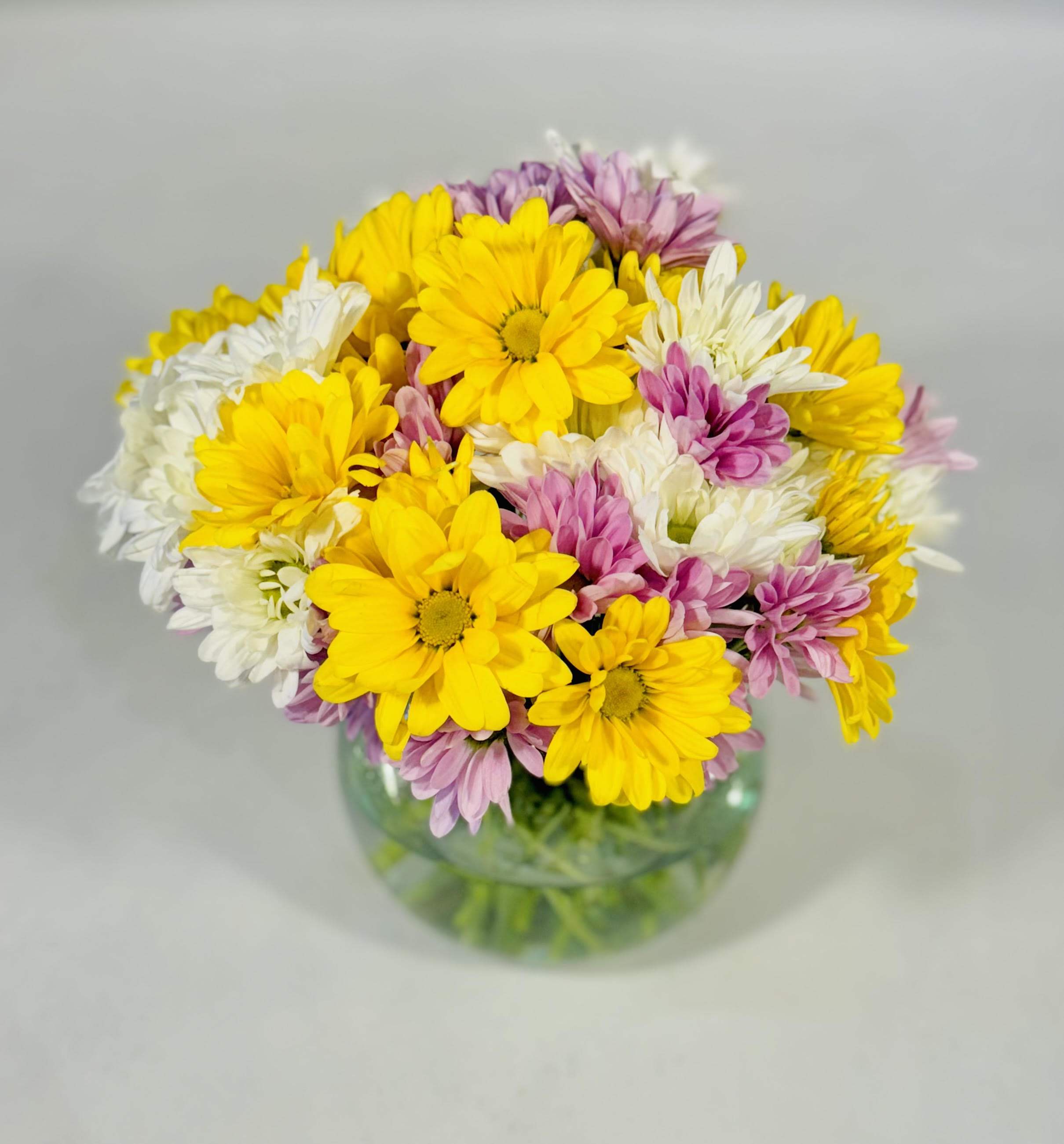 Bouquet of yellow, white, and pink daisies in a glass vase