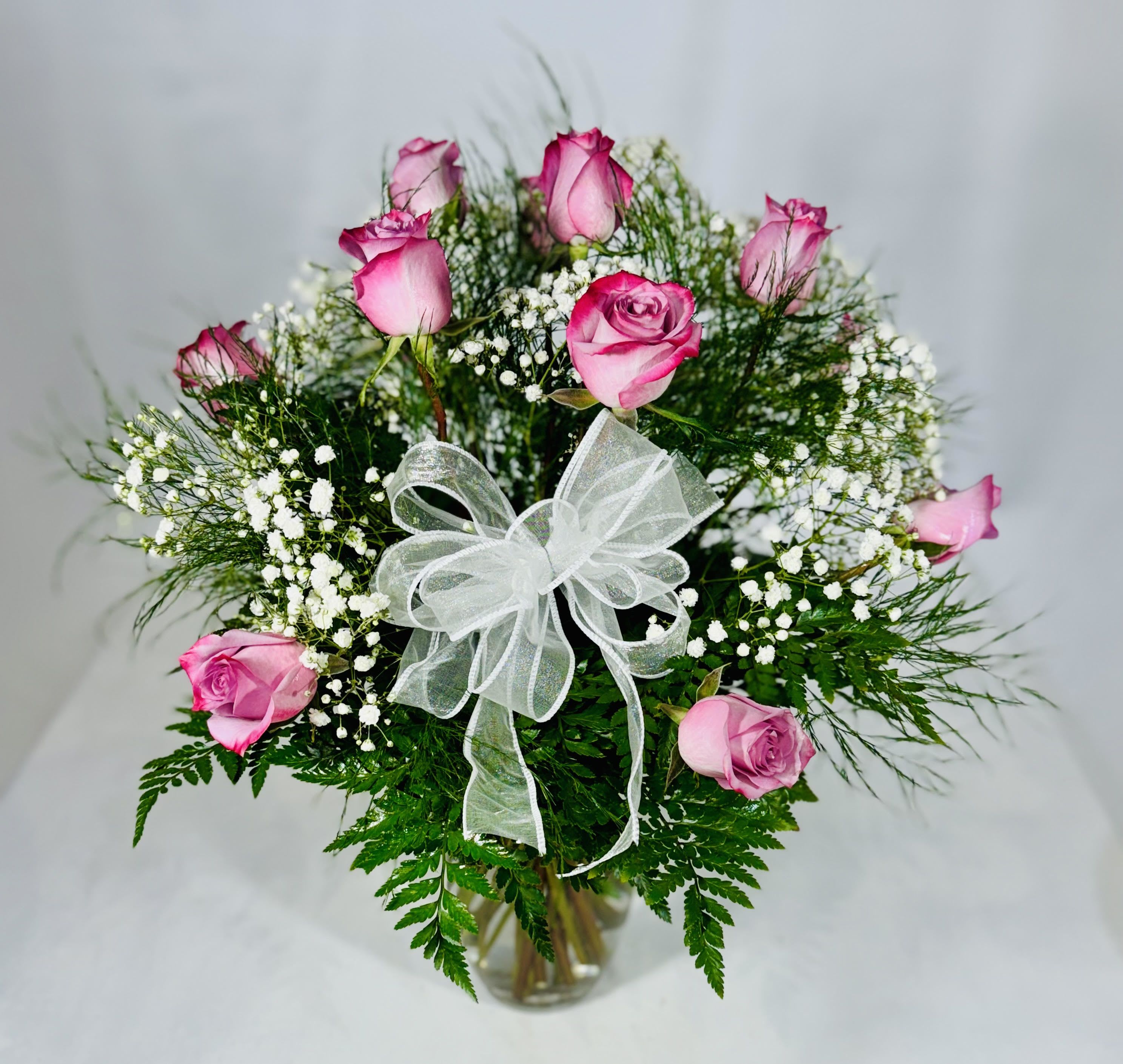 Pink roses in a clear vase with white baby's breath and a white ribbon bow