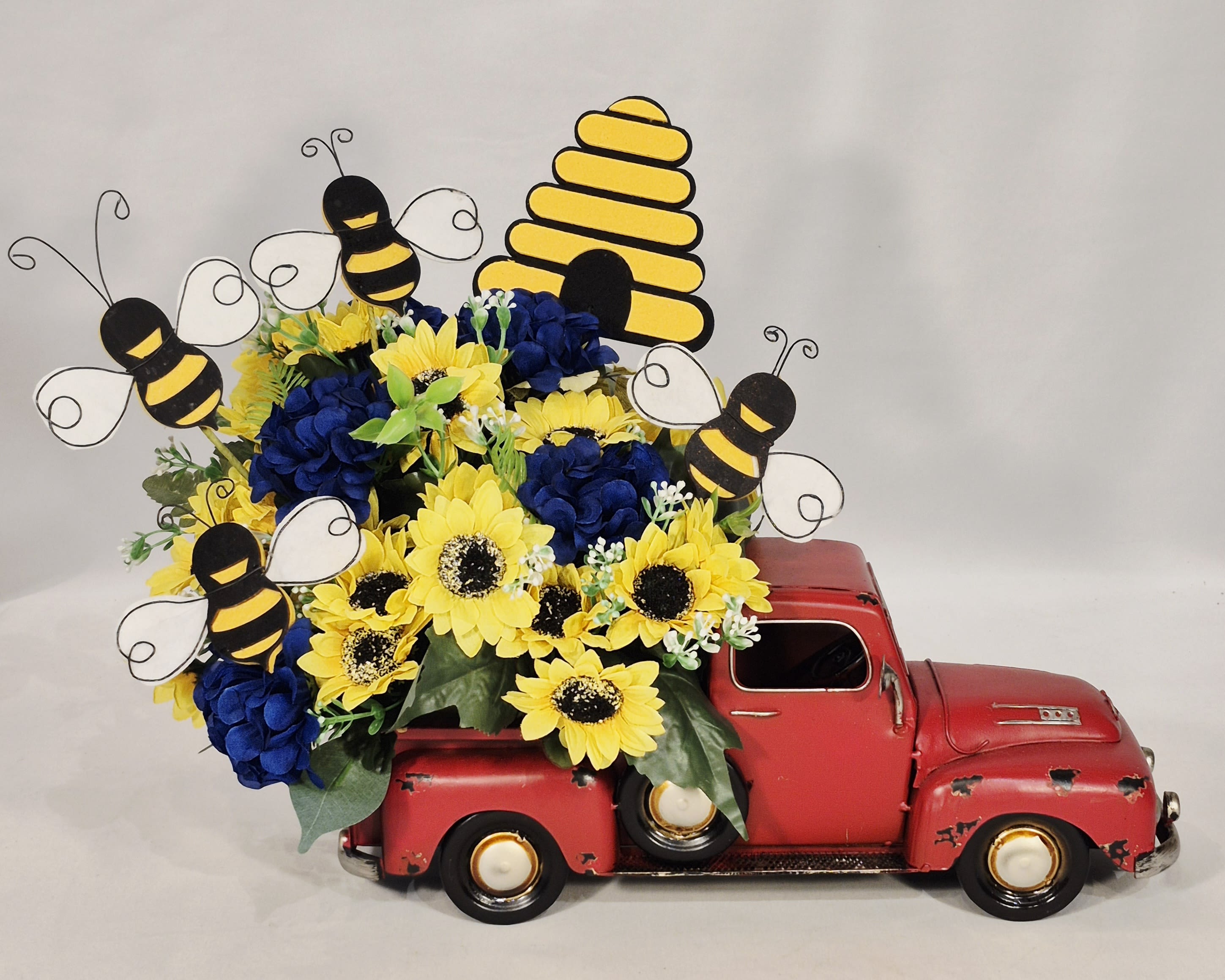Yellow sunflowers and blue hydrangeas arranged in a red toy truck with bee decorations