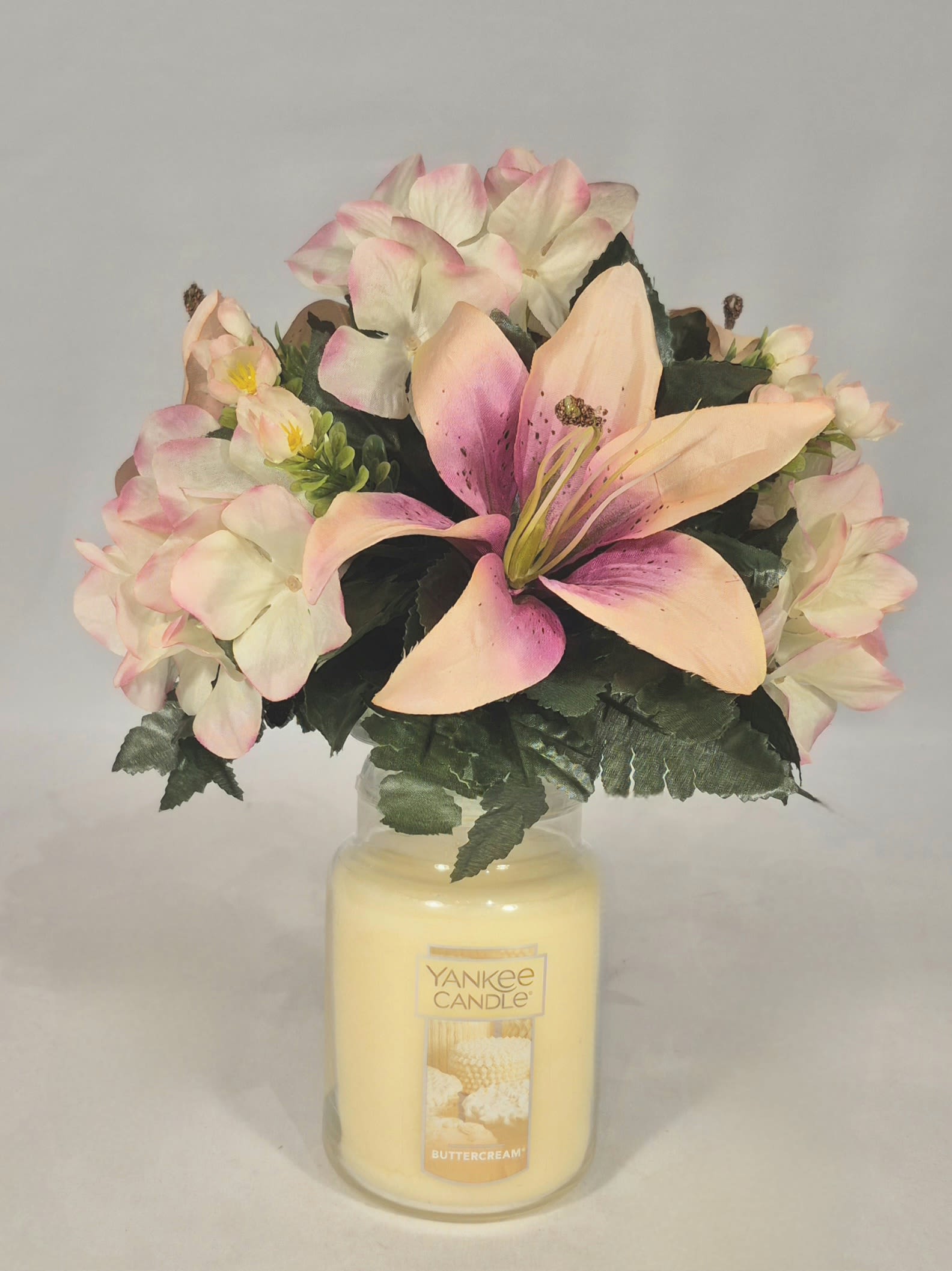Pink and cream flowers arranged in a glass candle jar