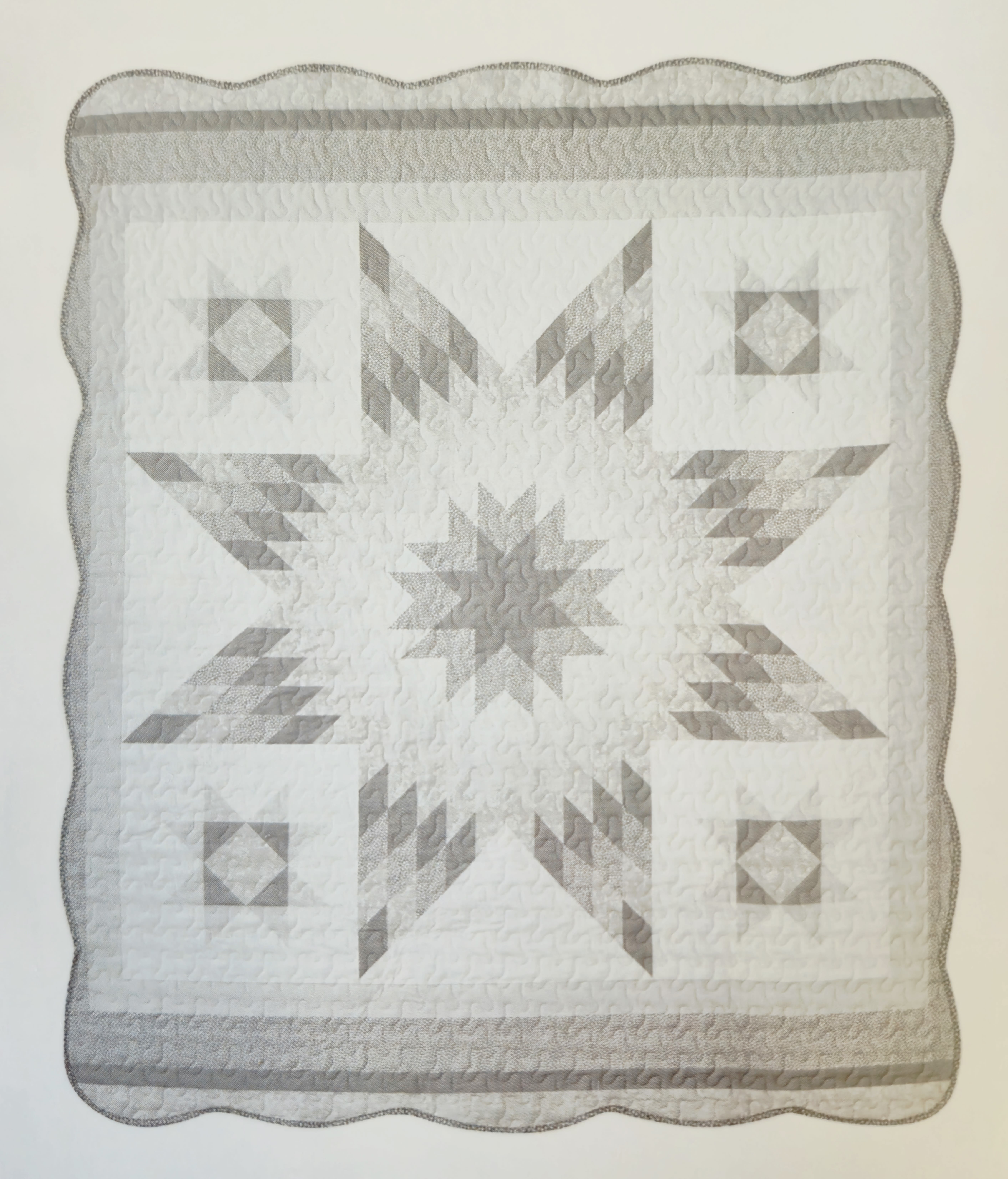 Grey &amp; White Star Pattern Quilted Throw  - A soft gray-and-white star quilted throw brings quiet comfort to any home - perfect as a housewarming gift or a thoughtful present for someone settling into a new apartment. This 50 x 60 quilted blanket reads like a cozy heirloom: the large central star motif framed by repeating geometric blocks gives a calm, traditional look that will appeal for everyday use or as a layered accent on a sofa or bed.  Hand-stitched texture and scalloped edges highlight the handmade feel: white, light gray, taupe-gray, and subtle darker accents work together for a neutral palette that blends with most décor. The visible quilting adds warmth and weight without bulk, and the 50 x 60 size is ideal for draping over a chair, foot of a bed, or curling up on the couch.  Machine wash gentle or spot clean as needed; its durable quilting holds up to regular use while keeping a timeless, cozy look.