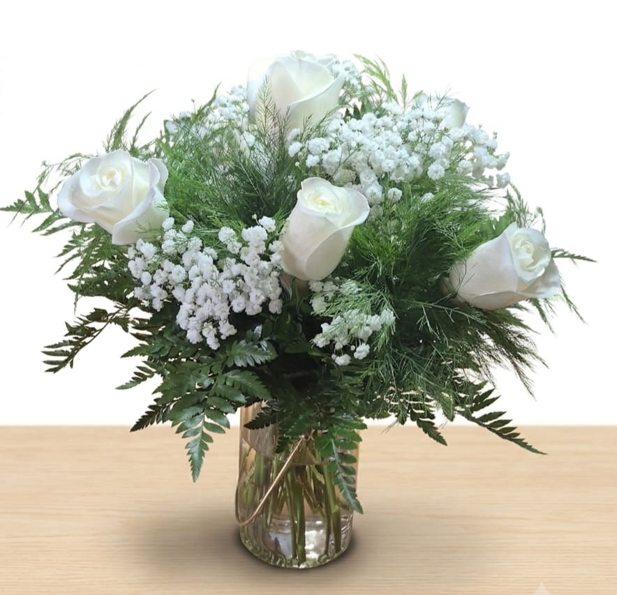 Half Dozen White Roses  - Crisp white roses arranged with delicate baby's breath and lush fern greenery create a calm, elegant bouquet perfect as a sympathy arrangement, a quiet celebration, or a thoughtful everyday gift. This half dozen white roses arrangement sends a message of peace and sincere care she'll feel comforted and seen by the clean, timeless palette of white and green.  The roses are clustered into a full, rounded design that highlights the contrast between the velvety white petals and deep green foliage. Accents of airy baby's breath add lightness and texture, while the clear glass vase keeps the presentation simple and classic. Arrangement stands approximately 9" tall in the vase, arriving ready to display.