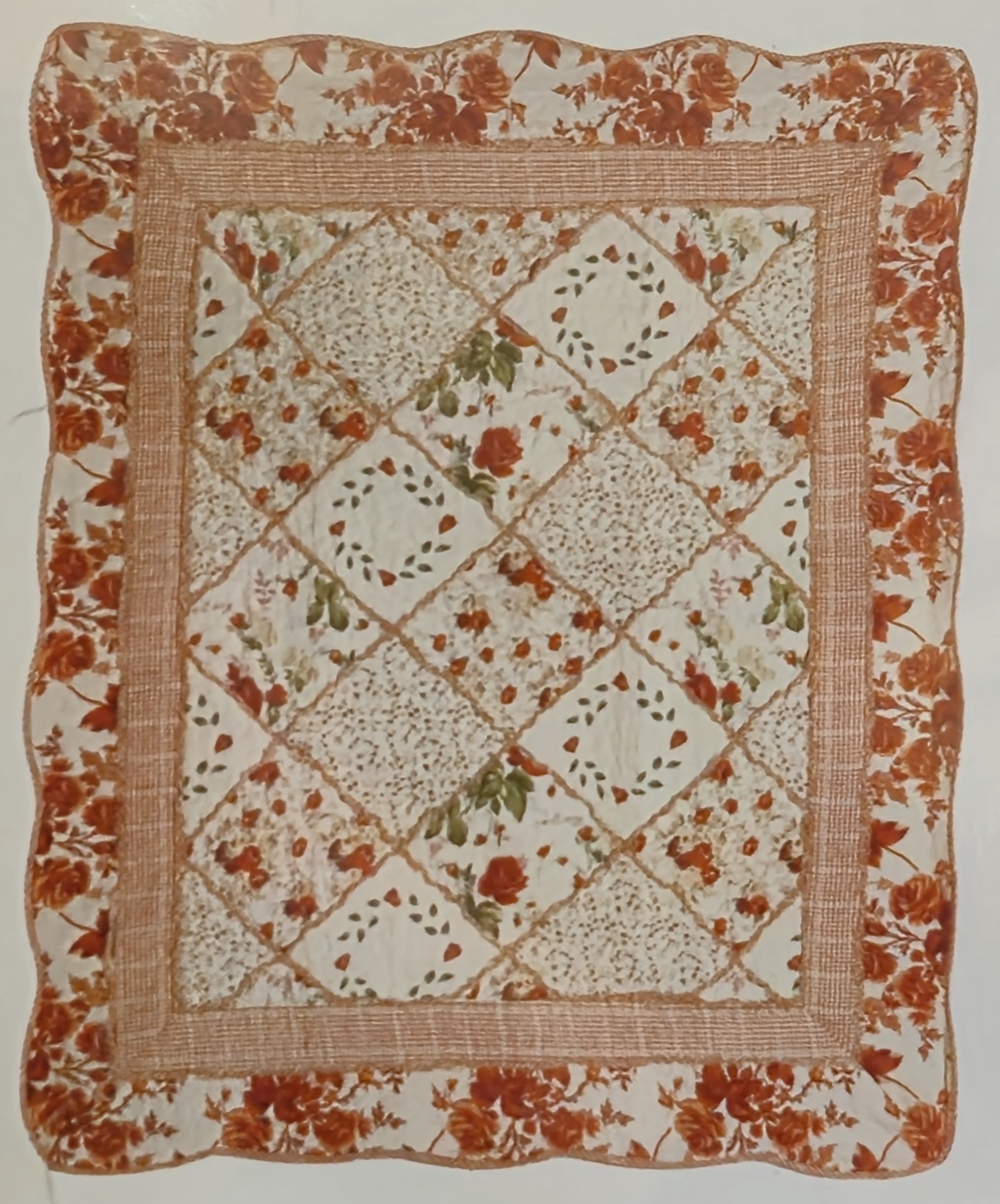 Burnt Orange &amp; Cream Quilted Throw  - A cozy, country-inspired square quilted throw in warm burnt orange and cream brings a heartfelt, handmade look to sympathy displays or seasonal home décor. This quilted style throw works well as a comforting accent for a memorial service or to send as a thoughtful remembrance gift the warm hues and soft patterning convey care and gentle warmth to the person you're thinking of.  The patchwork-style floral print mixes small rose-like motifs, scattered sprigs and diamond-shaped panels in orange-red, cream and subtle green accents, all framed by a textured stitched border for added depth and a layered, stitched appearance. The padded, rounded edges and fabric trim give it a soft, tactile feel that reads as decorative rather than formal.  For a more formal presentation, choose the Deluxe option and we will mount the quilt on a simple, neutral metal easel stand (adds an elevated display perfect for services or receptions). 