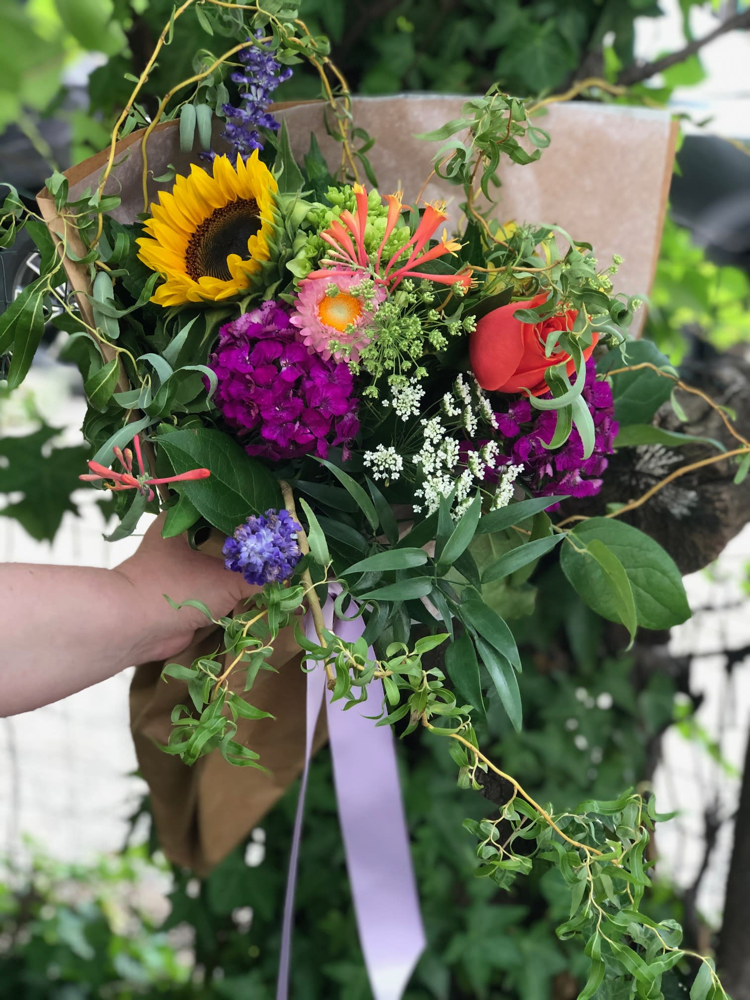 Hand-tied bouquet with a sunflower, red rose, and purple blooms