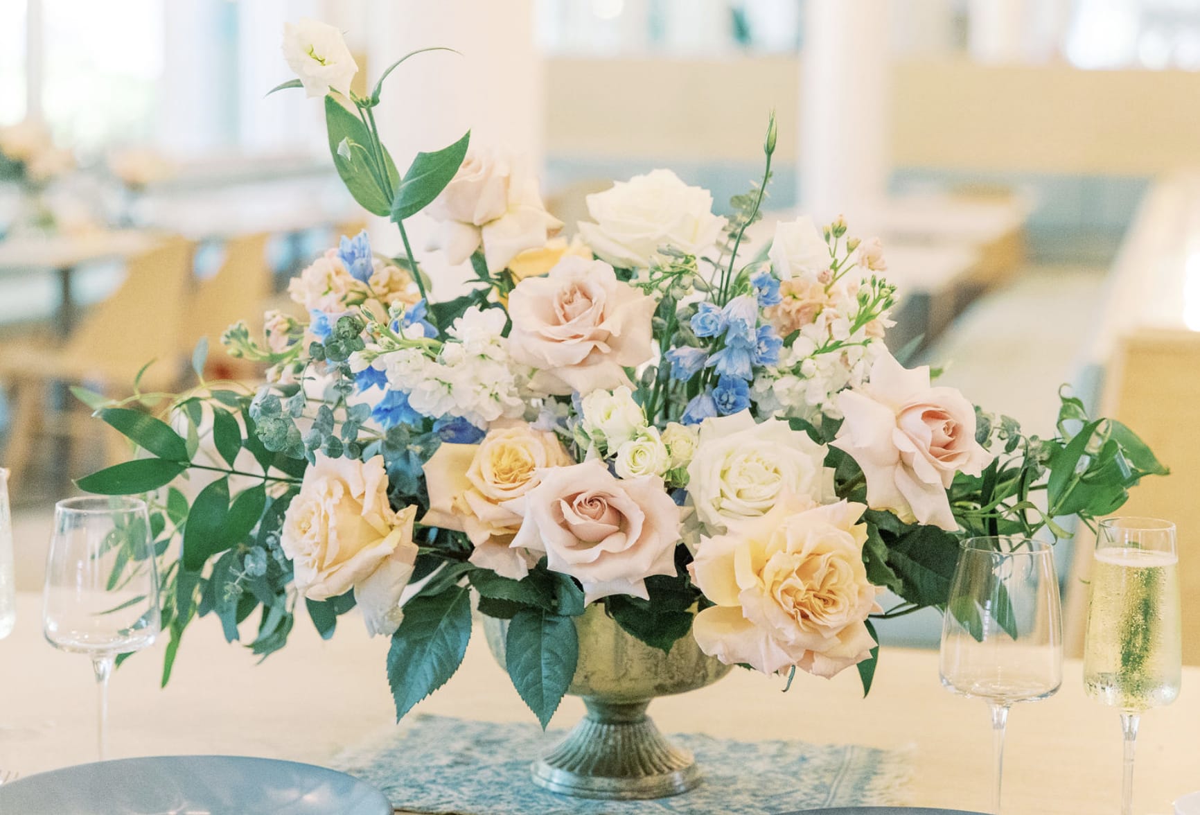 Pastel rose centerpiece in a pedestal vase with blue and white flowers