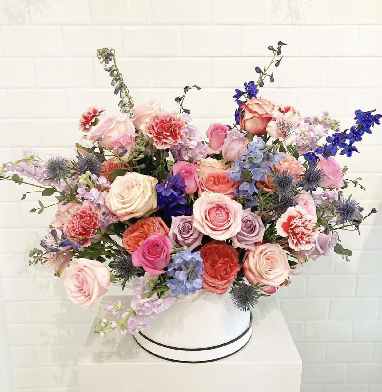 The Marie Antoinette  - Set aside your chapeaus and indulge in the luxury of this elegant floral hat box. Treat someone like a queen for the day with this show-stopping arrangement, featuring a stunning mix of pink and purple roses, delphinium, stock, carnations, and a touch of thistle — a color combination that can’t be beat!