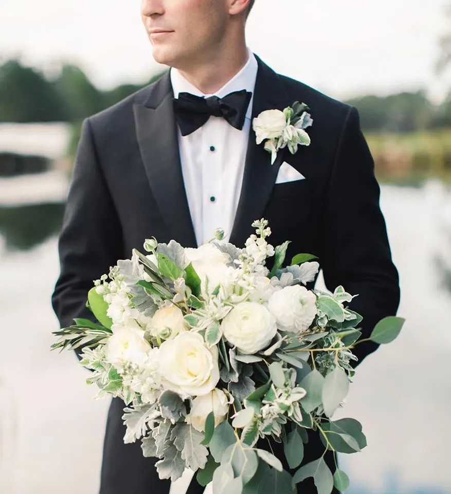 Man in tuxedo holding a white bridal bouquet with greenery