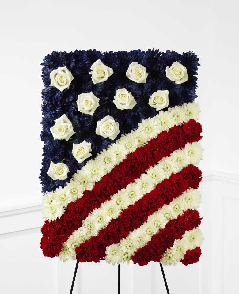 The FTD Glory Be Flag Tribute - The FTD Glory Be Flag Tribute is a symbol of patriotic beauty to commemorate the life of your loved one at their final farewell service. Red carnations, white chrysanthemums and blue dyed white chrysanthemums create a stirring arrangement in the likeness of the American flag with white rose accents to symbolize the stars. Displayed on a wire easel, this exquisite arrangement will bring comfort and peace to their family and friends.