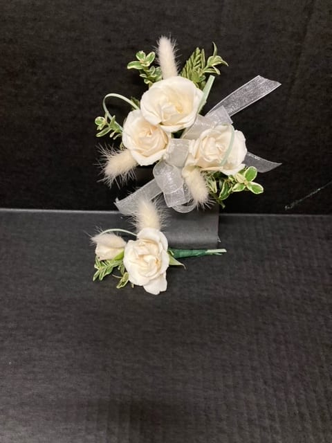 White rose corsage and boutonniere with ribbon on a dark background
