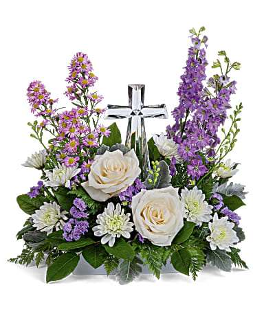 White roses and purple flowers arranged around a clear glass cross