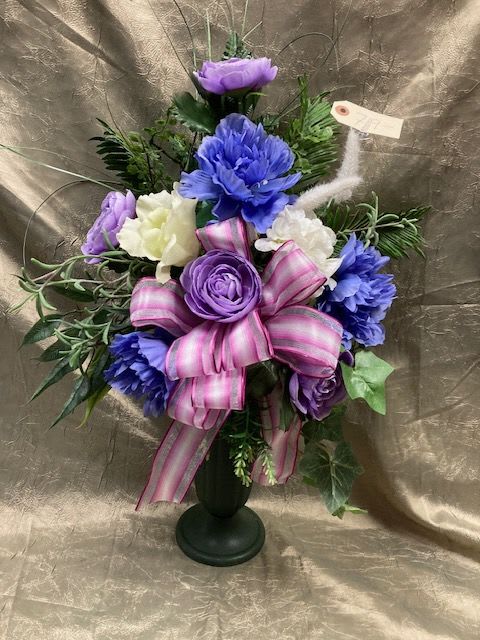 Purple and white floral arrangement in a black vase with a pink ribbon