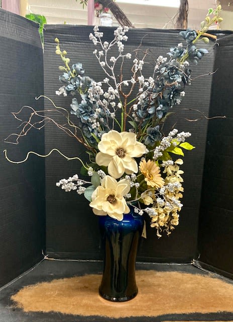 Tall floral arrangement in a blue vase with cream blooms and blue accents