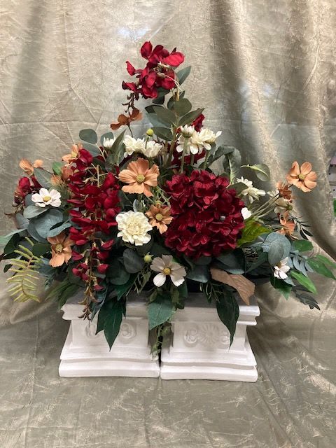 Red and peach floral arrangement in a white pedestal container