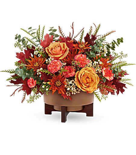 Autumn floral arrangement with orange roses and red blooms in a low container