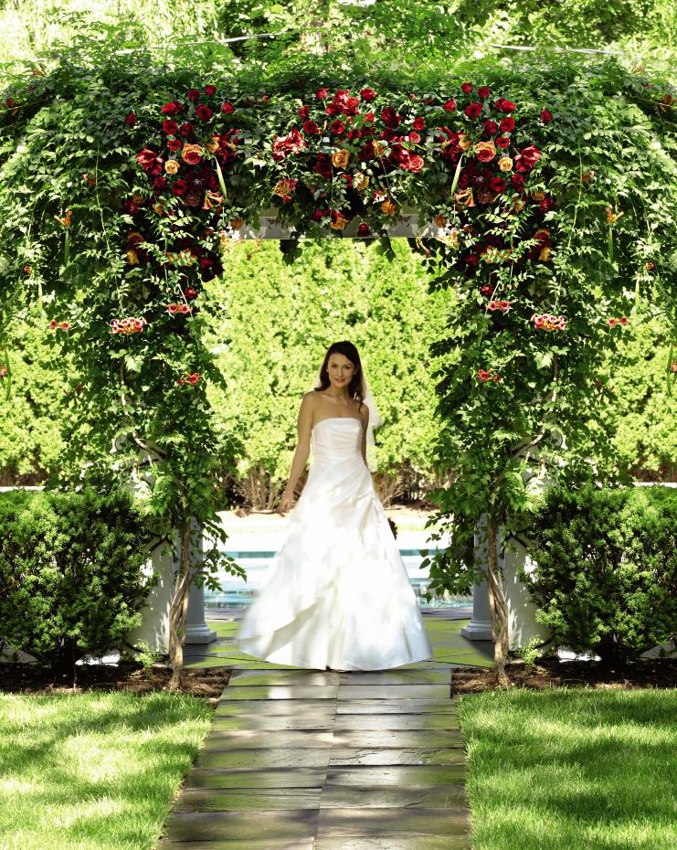 Bride in a white gown under a floral arch of red and orange roses