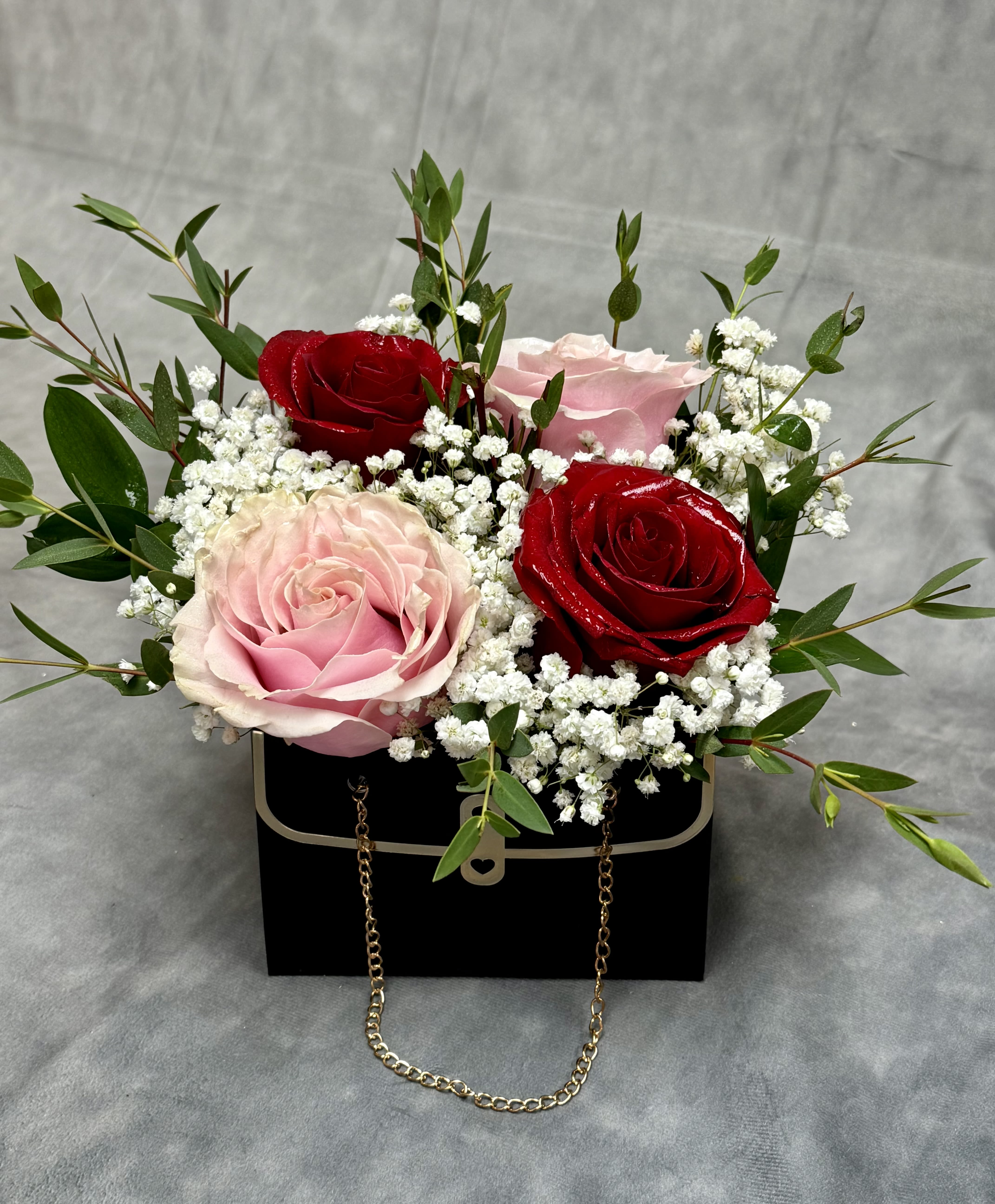 Pink and red roses arranged in a black box with white filler flowers
