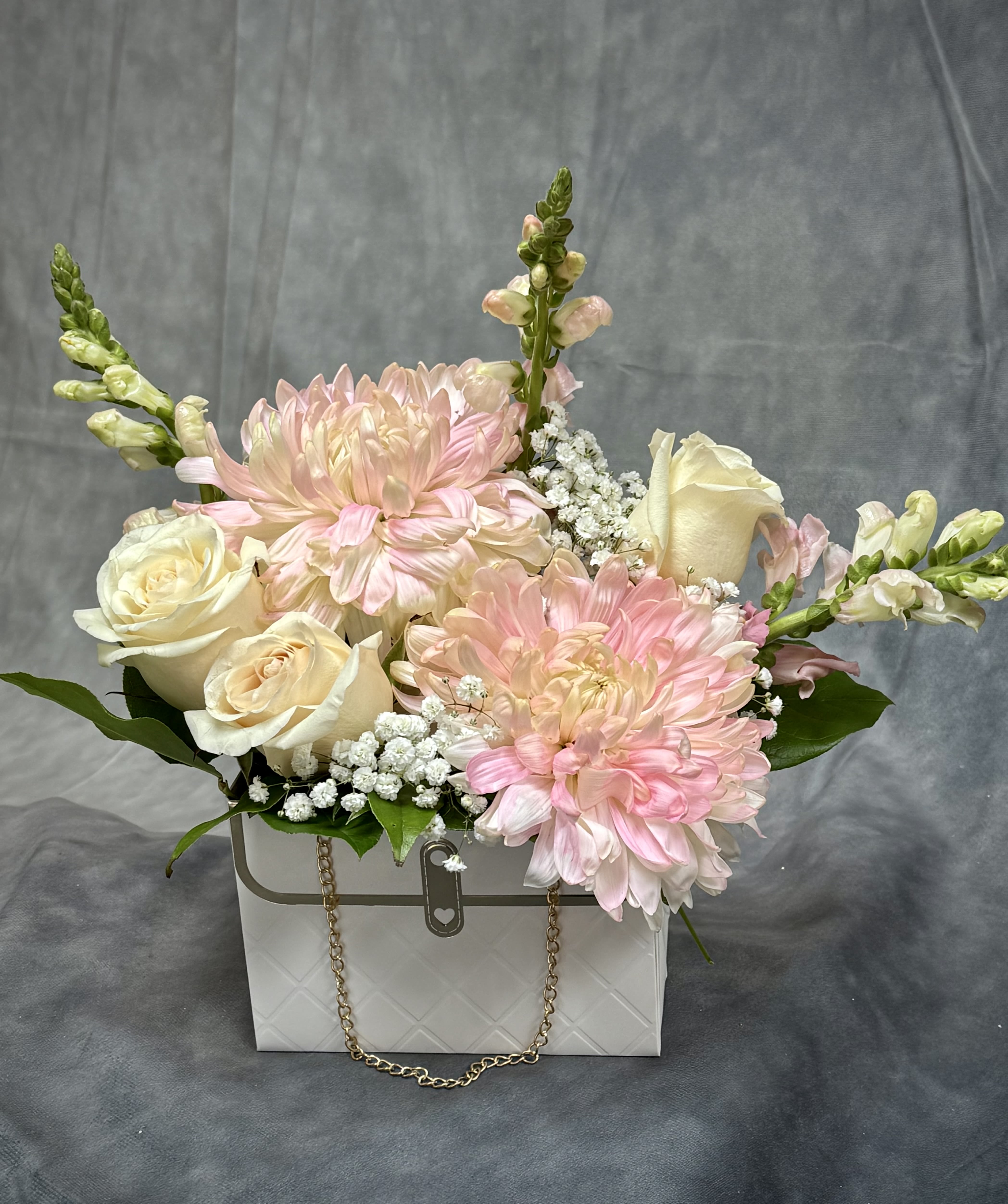 Pink and cream flowers arranged in a white gift box with a chain handle.