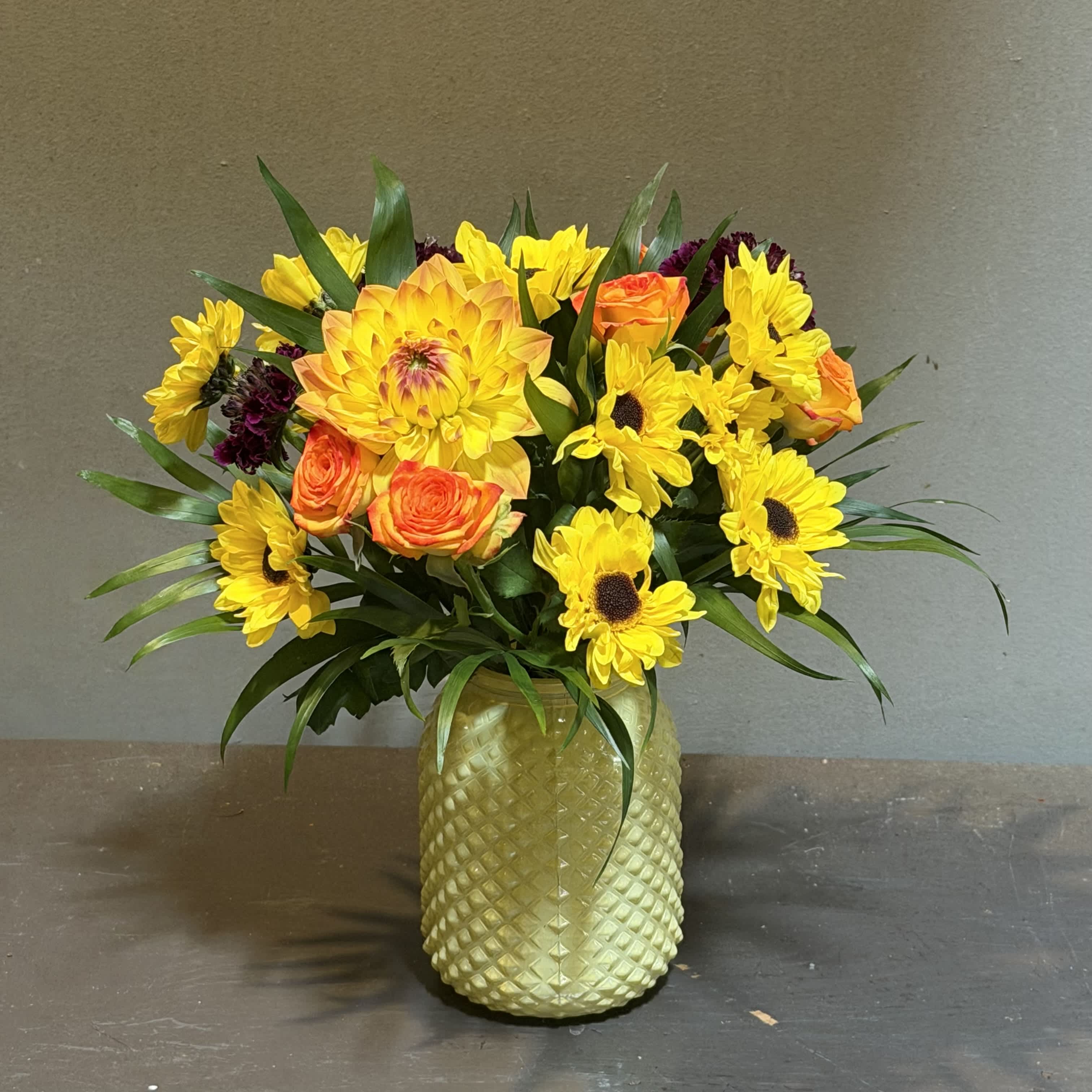 Yellow sunflowers and orange roses arranged in a textured vase
