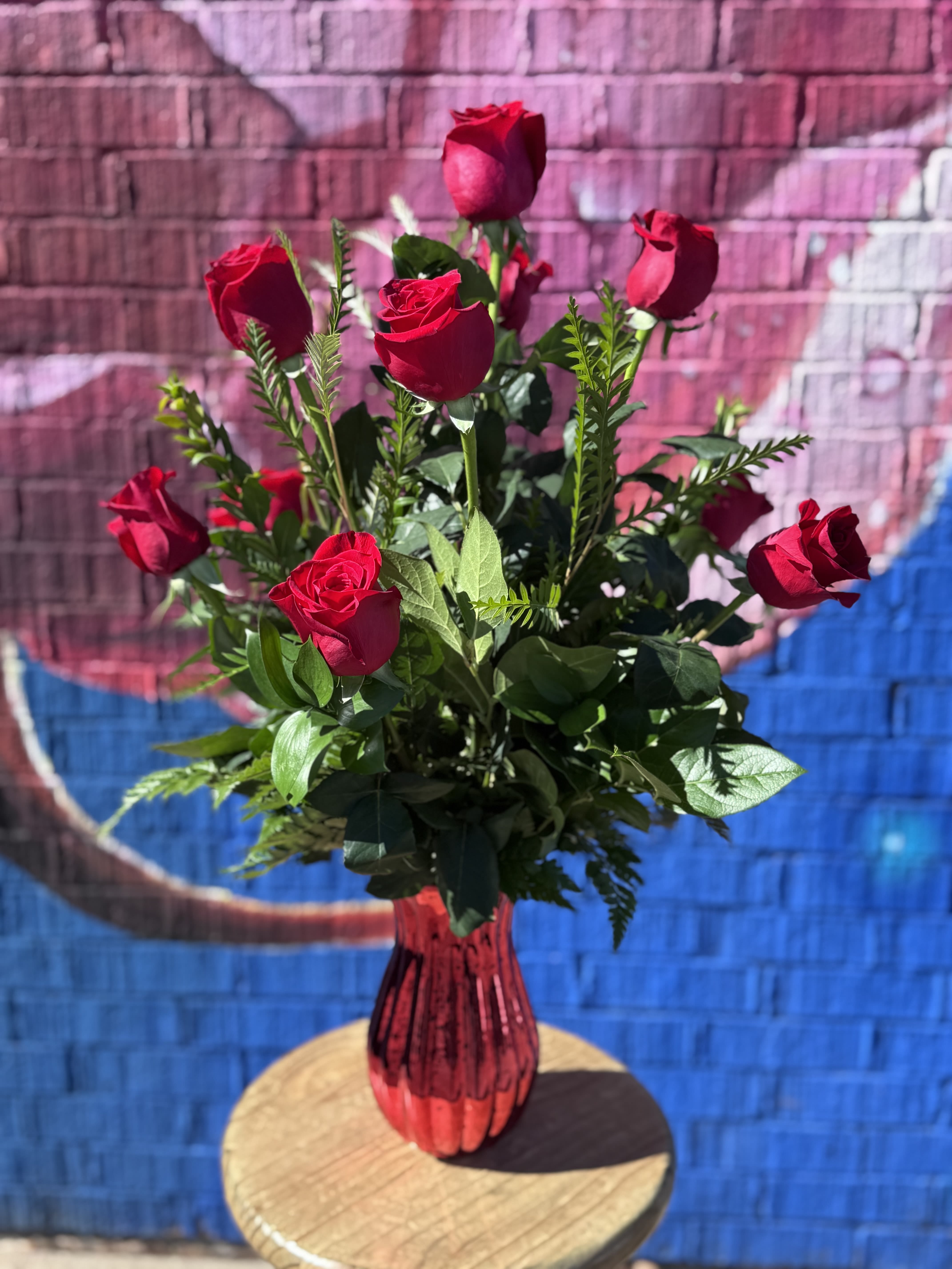 Tall arrangement of red roses in a shiny red vase on a small round table