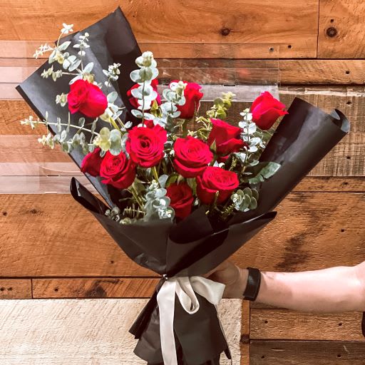 Bouquet of red roses with eucalyptus wrapped in black paper and tied with a white ribbon
