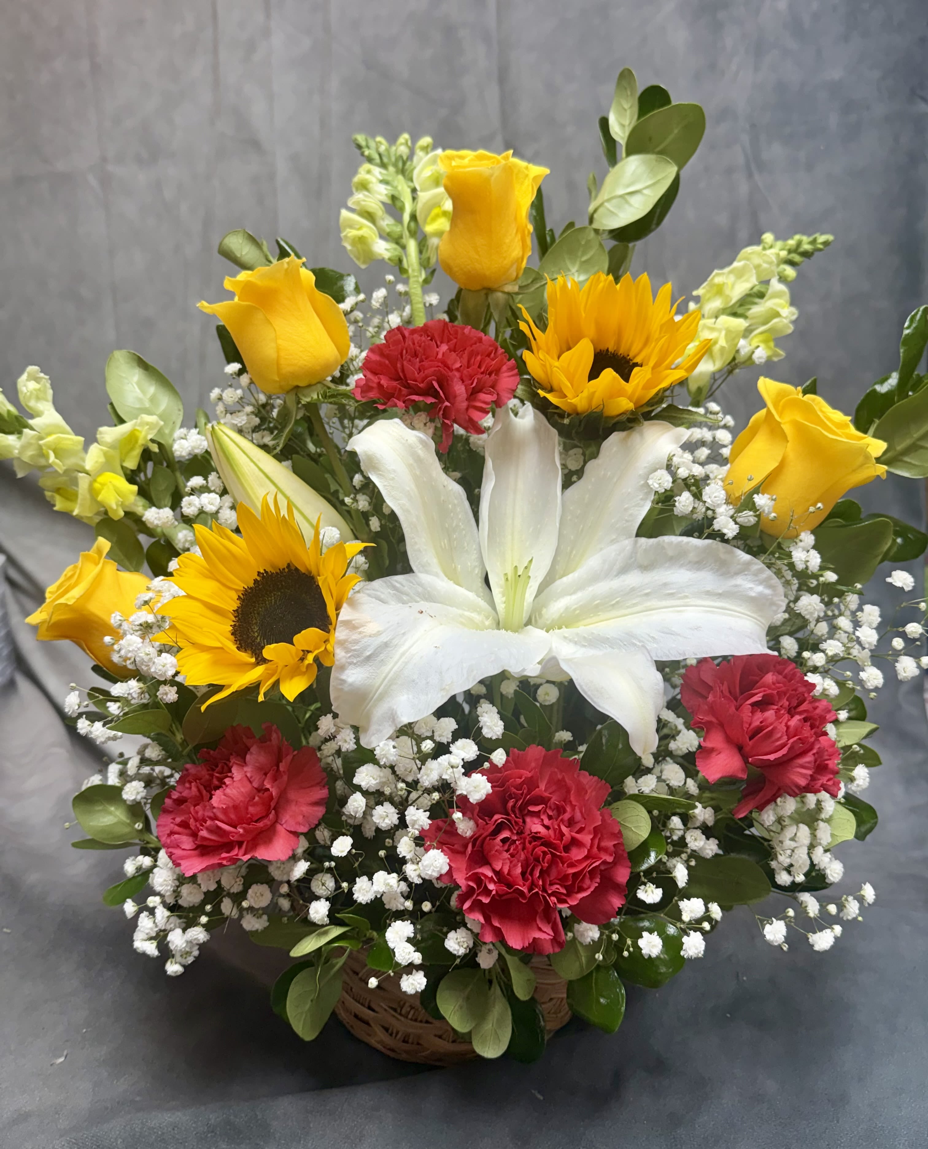 Basket arrangement with white lily, yellow roses, sunflowers, and red carnations