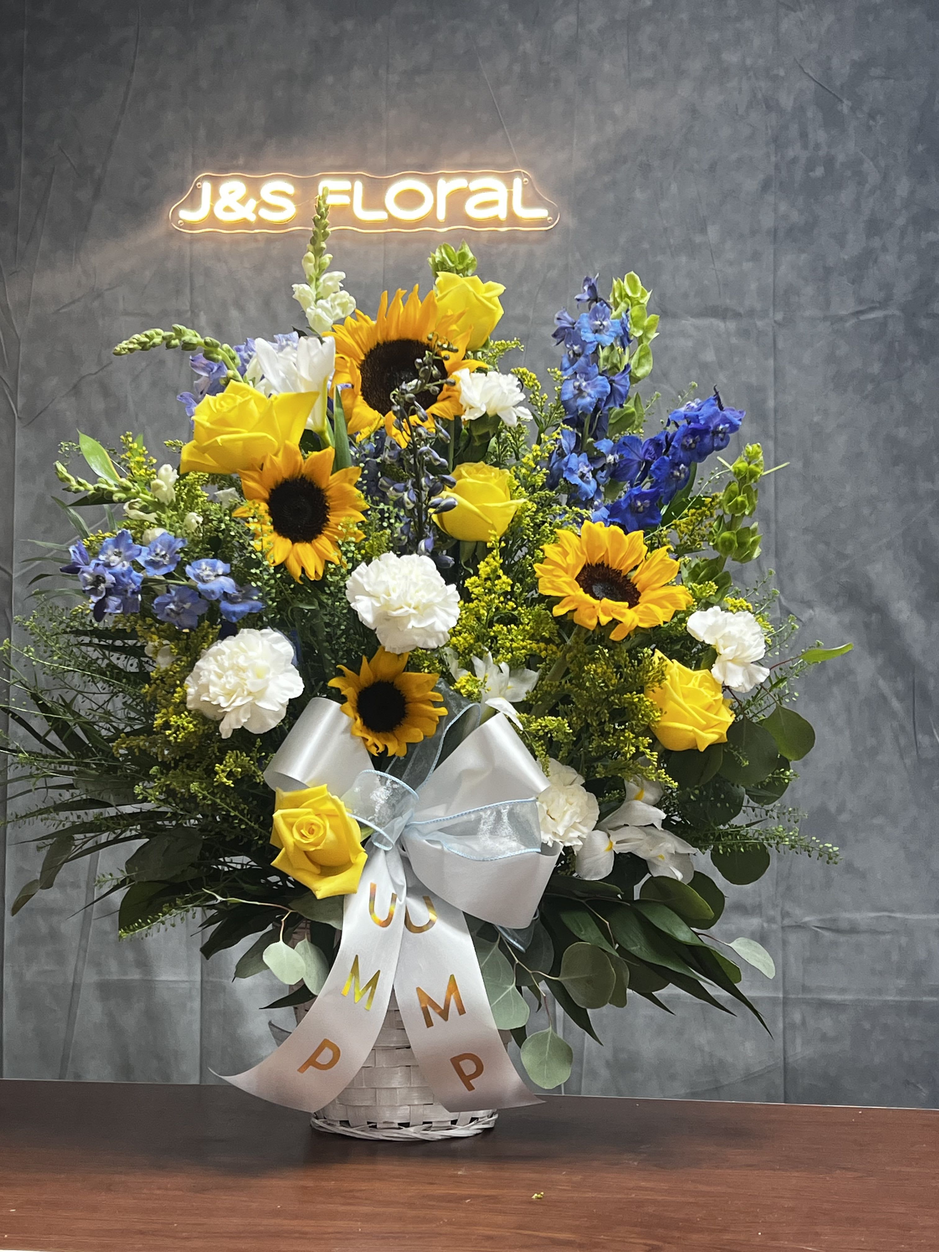 Basket arrangement with sunflowers, yellow roses, white carnations, and blue flowers