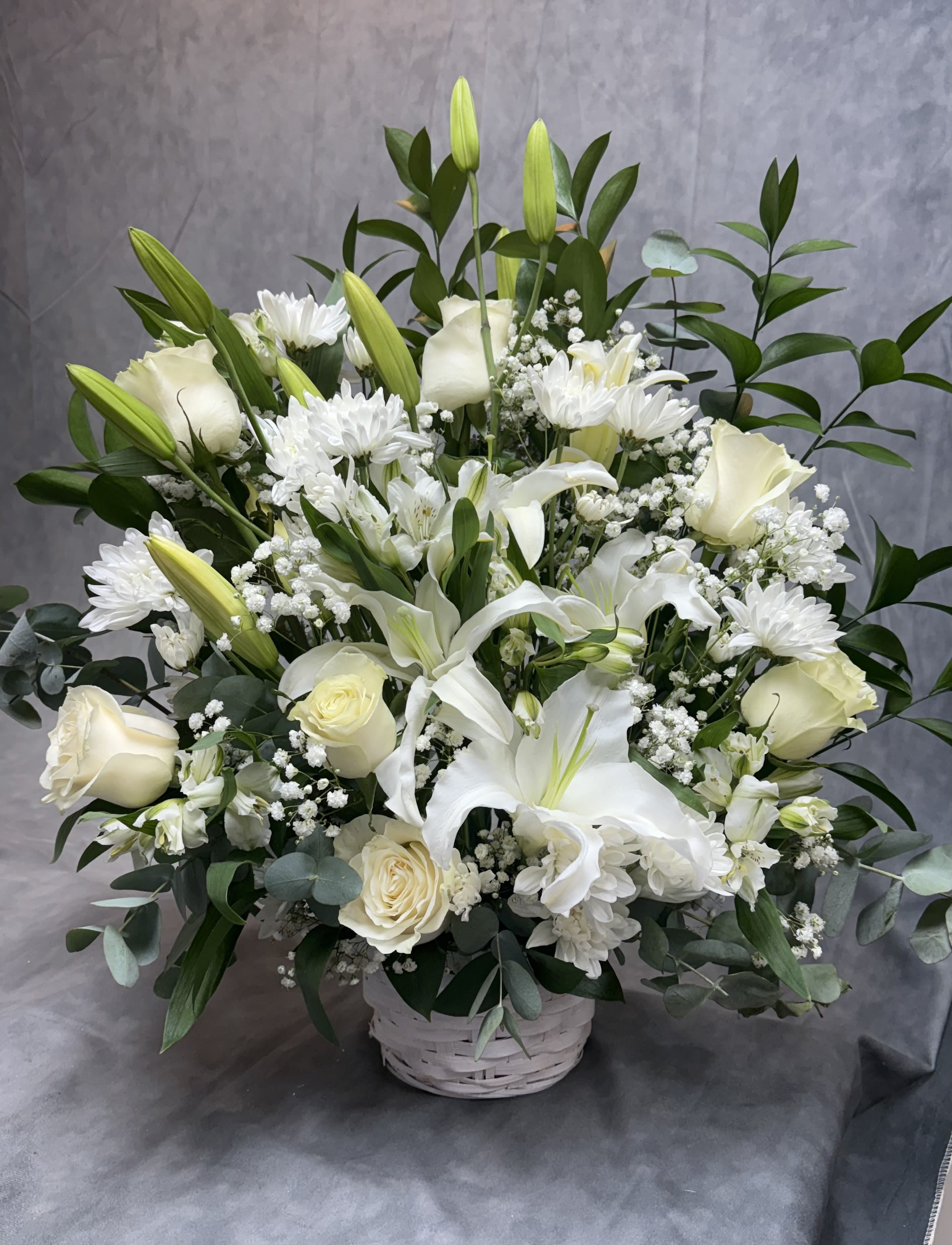 White lilies and roses arranged in a white basket