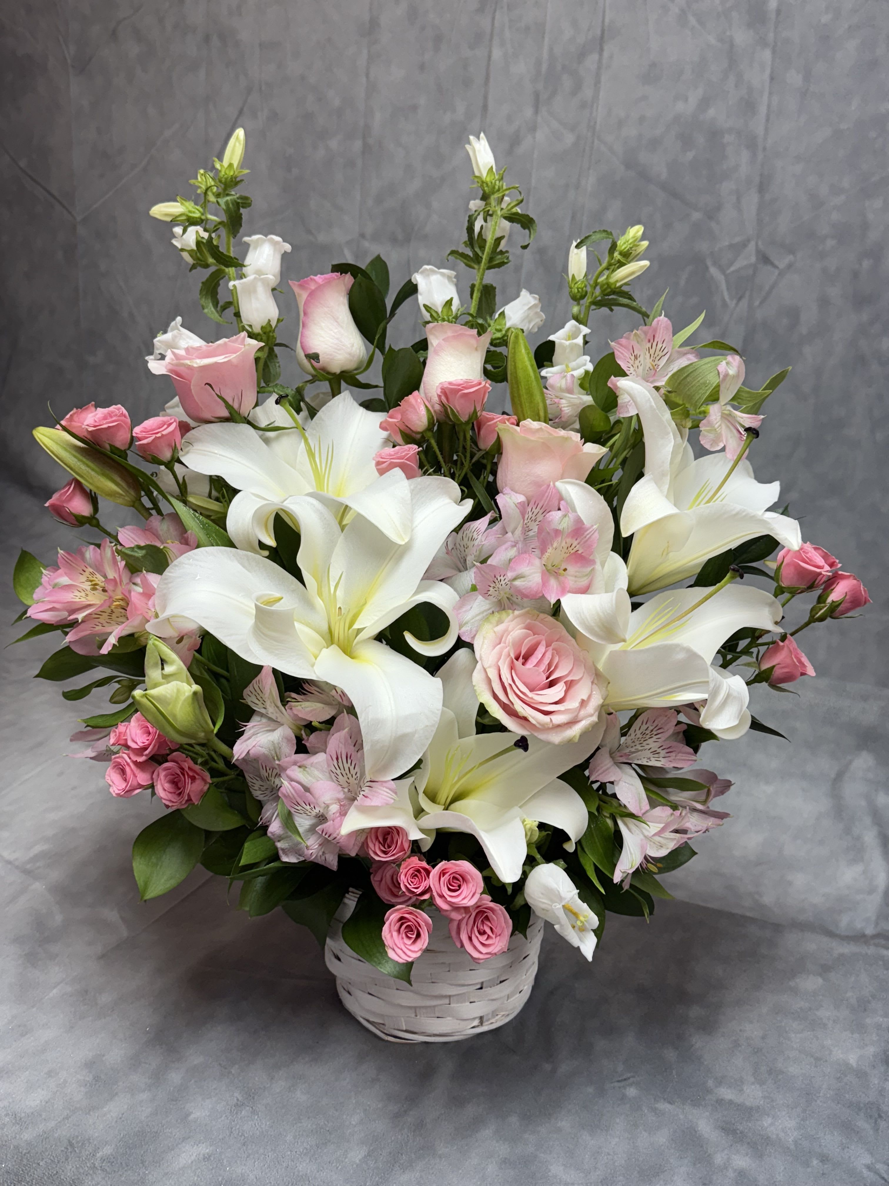 Pink roses and white lilies arranged in a white basket