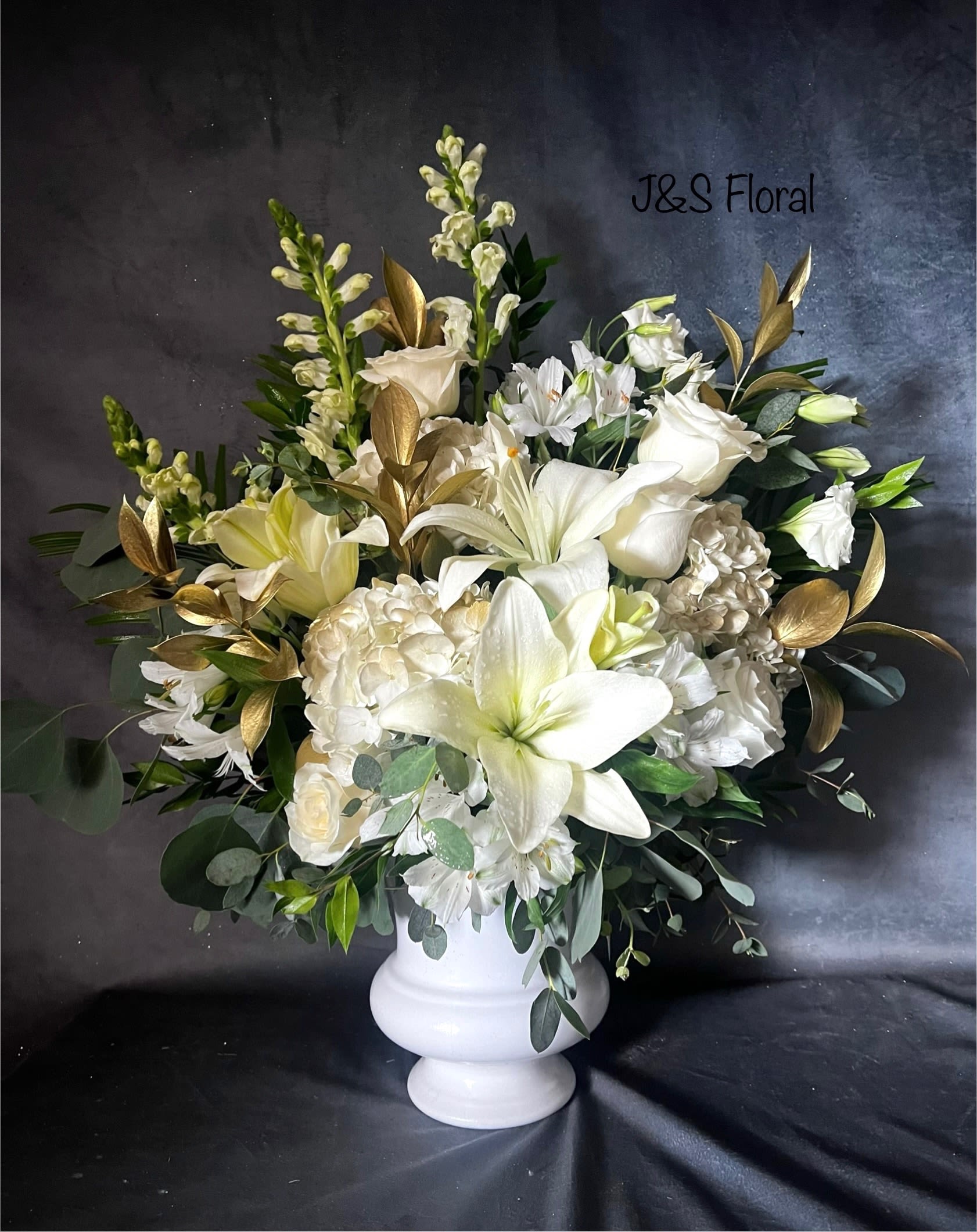 White floral arrangement in a white pedestal vase with gold foliage accents