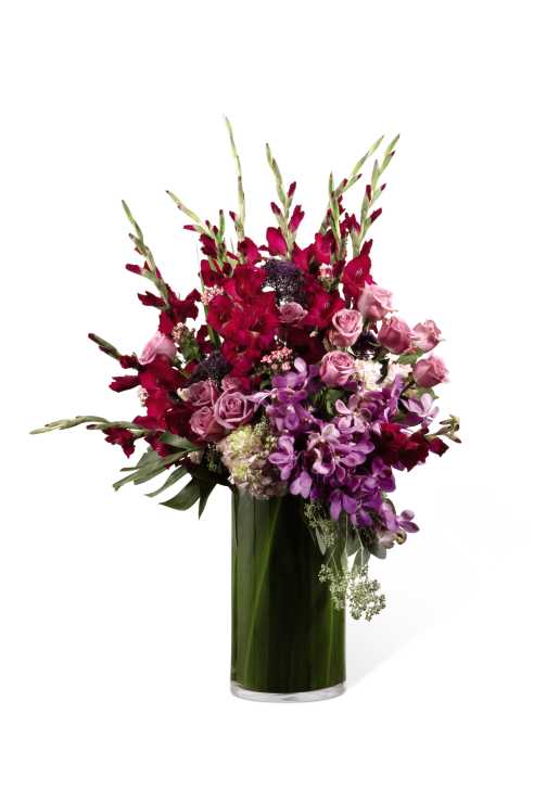 The FTD Quiet Tribute Arrangement - The FTD Quiet Tribute Arrangement is a sophisticated display of color and beauty that will bring an unmatched elegance to their final farewell service. Lavender roses, purple liatris, magenta gladiolus, purple dendrobium orchids, pink Asiatic lilies, pink hydrangea and purple larkspur are brought together in a clear glass cylinder vase lined with ti leaves to create a stunning presentation of blushing serenity that gorgeously honors one who will always be missed.