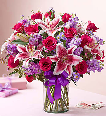 Bouquet of pink roses and lilies in a glass vase with a purple ribbon