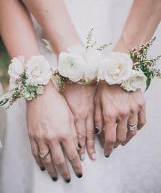 Hands wearing white floral wrist corsages with small white blooms