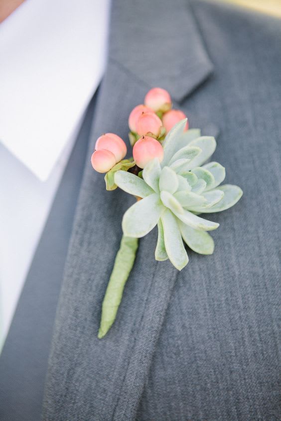 Succulent boutonniere with pink berries pinned to a gray suit lapel