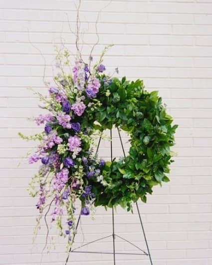 Large floral wreath with purple blooms and dense green foliage on a stand