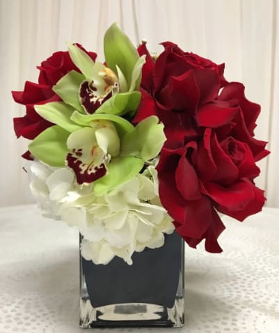 Red roses, green orchids, and white hydrangeas in a square glass vase