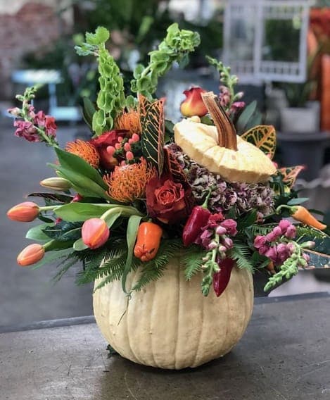 Autumn floral arrangement in a pumpkin-shaped container with roses and tulips
