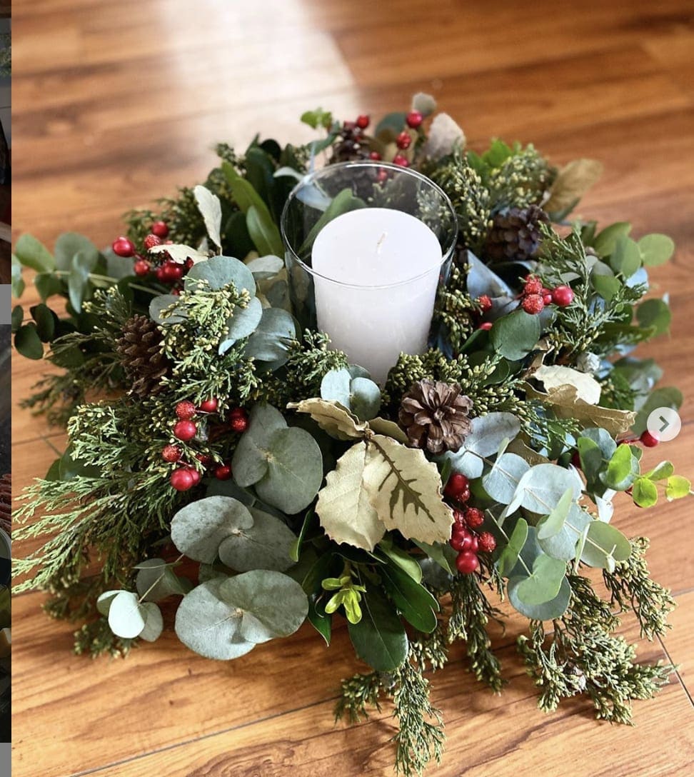 Candle in a glass holder surrounded by a holiday greenery wreath