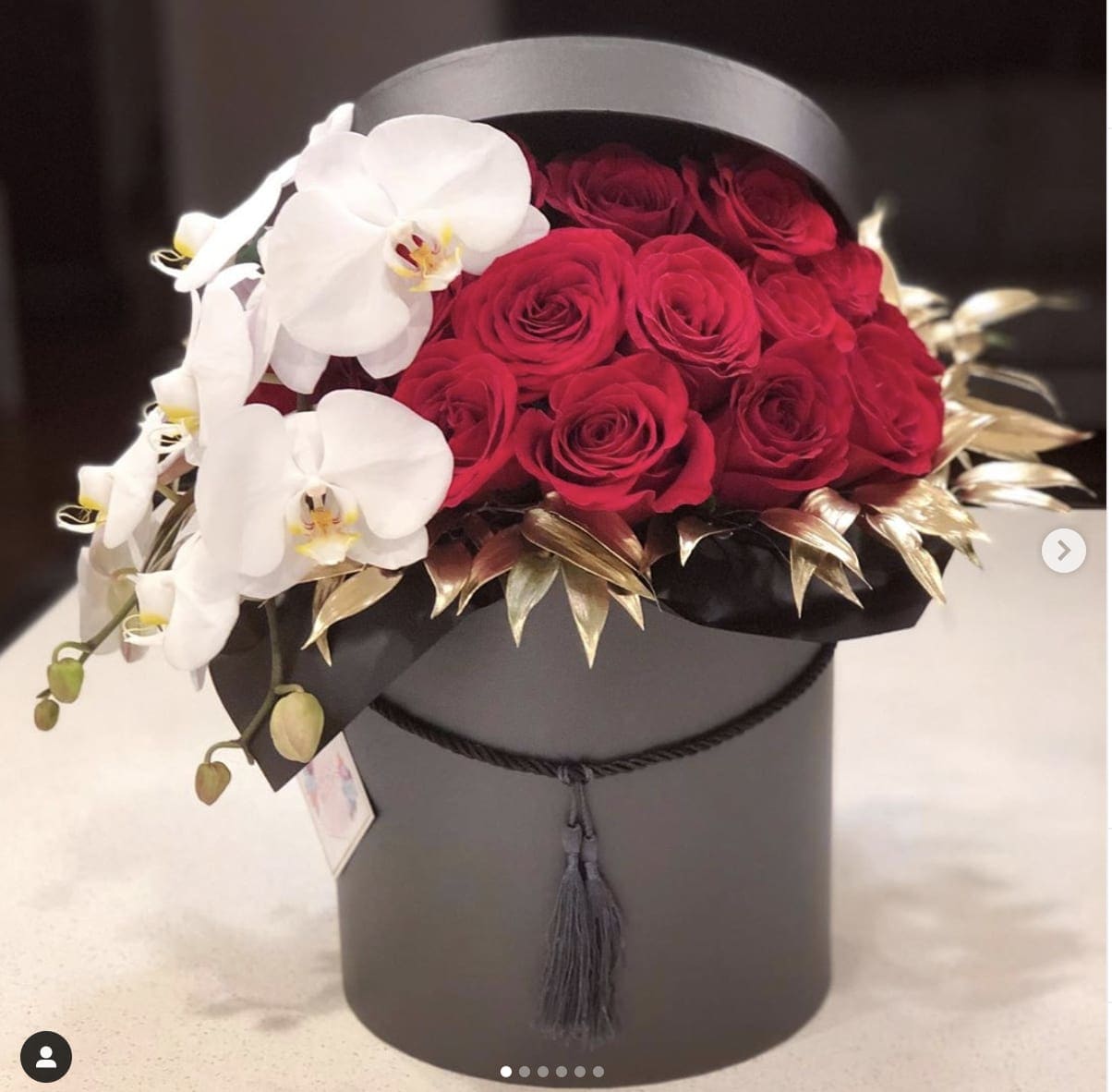 Red roses and white orchids arranged in a black hat box