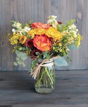 Mixed bouquet of orange, yellow, and white flowers in a glass jar
