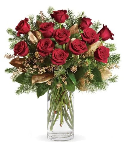 Red roses arranged in a clear glass vase with evergreen accents