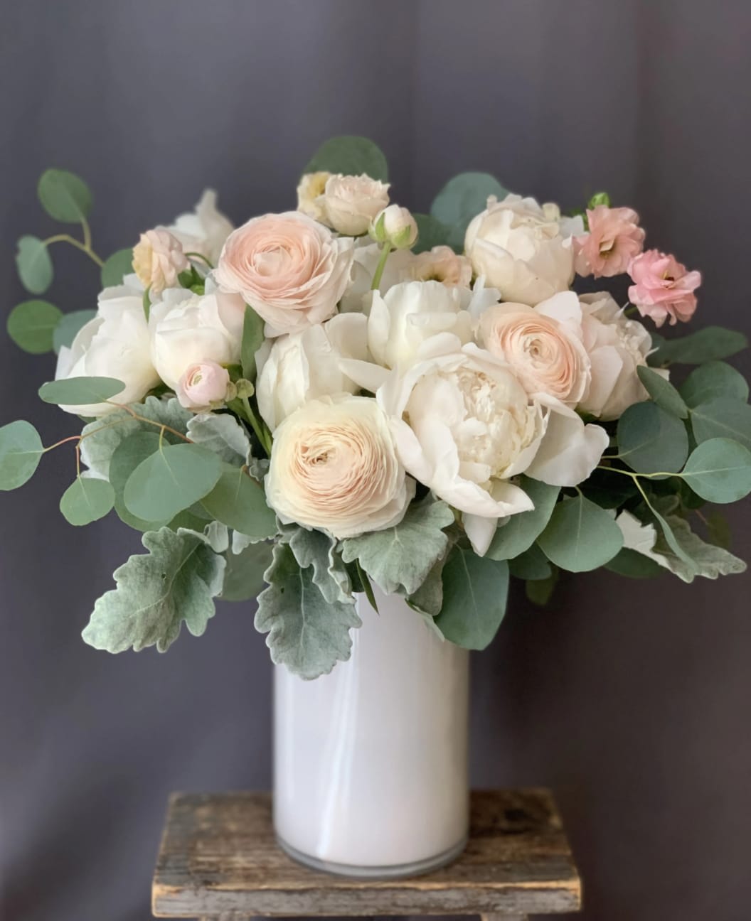 Blush and white bouquet in a white vase with round green foliage