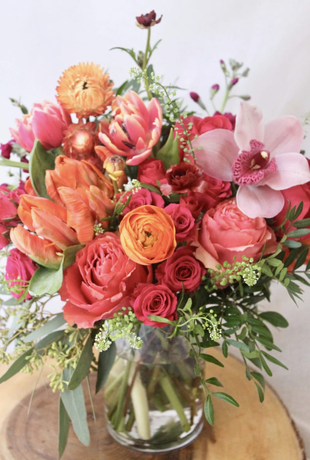 Mixed bouquet of pink, orange, and red flowers in a glass vase