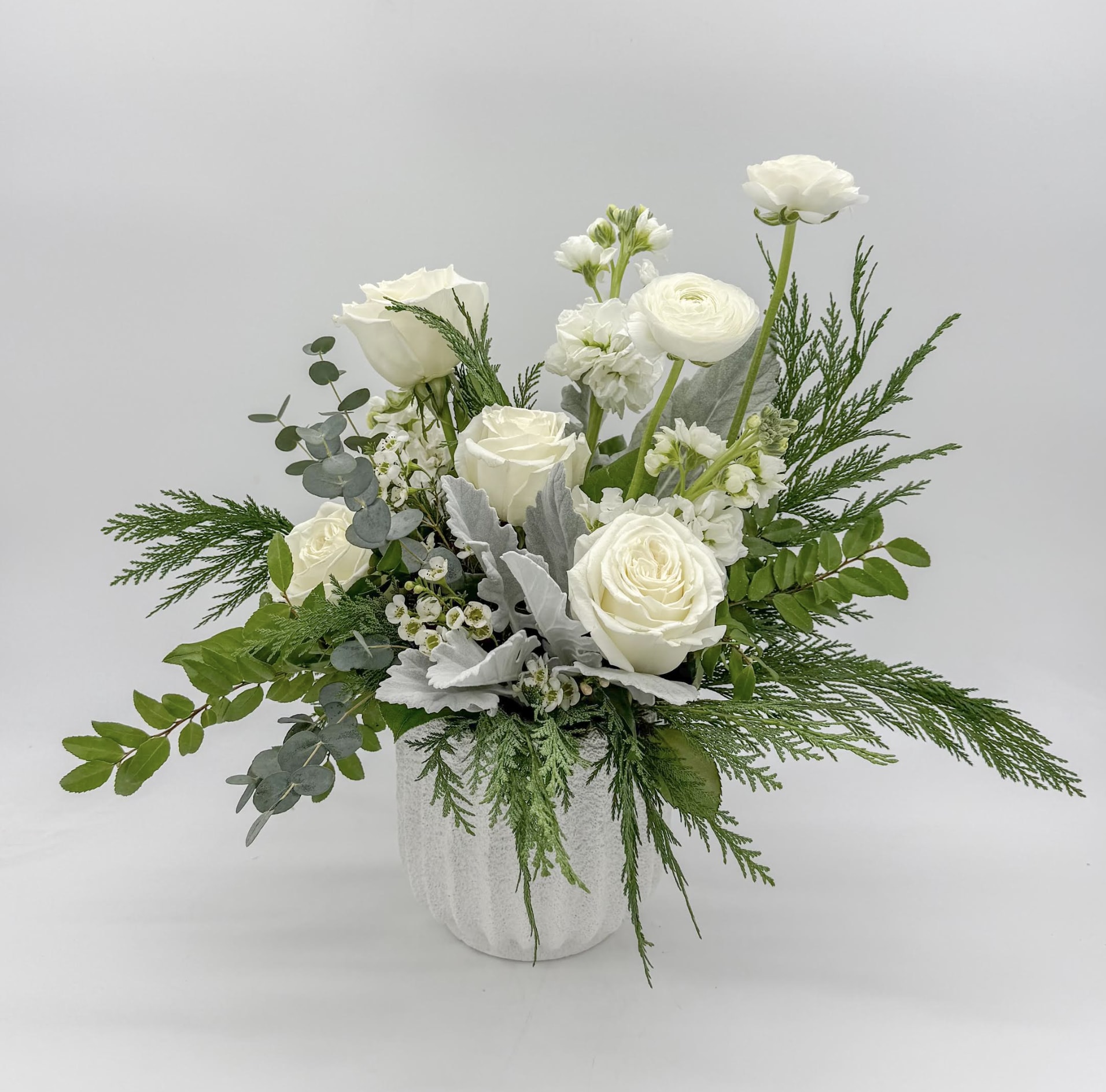 White roses and ranunculus in a white vase with mixed greenery