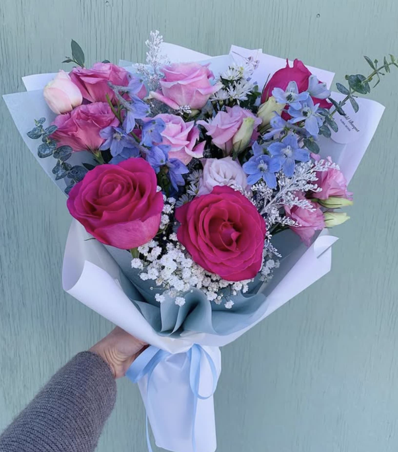 Bouquet of pink and blue roses with white filler flowers wrapped in white paper