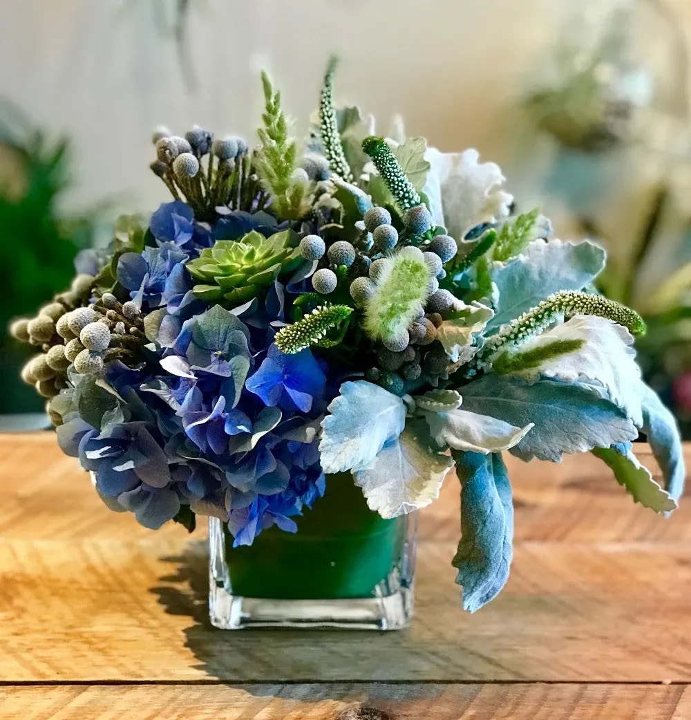 Blue and green floral arrangement in a square glass vase