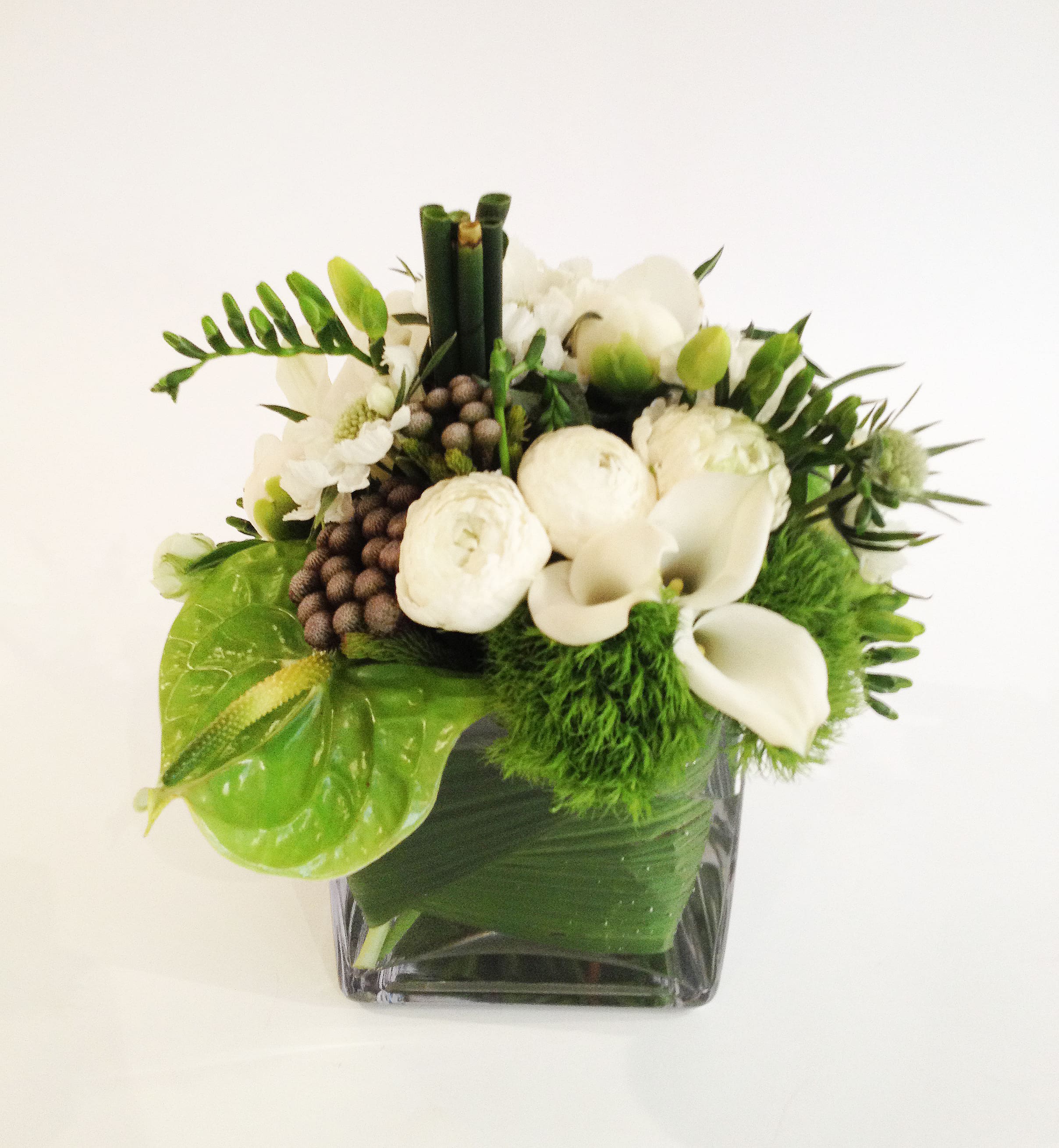White flowers and green accents arranged in a square glass vase