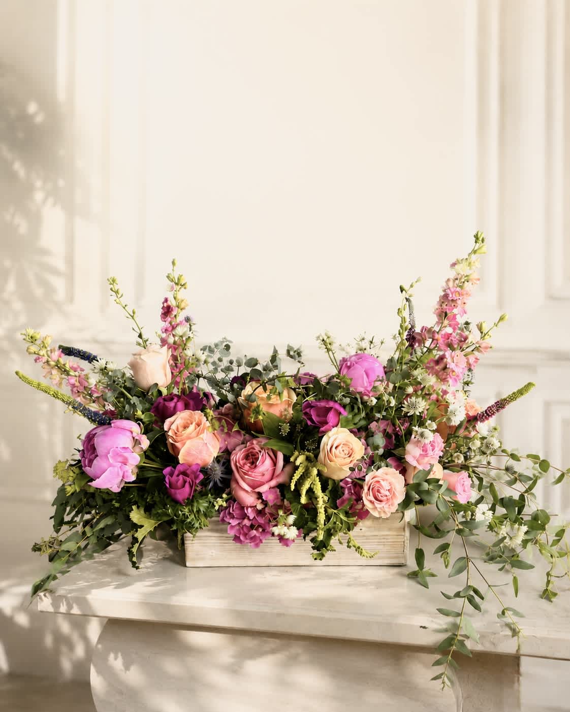 Low floral arrangement of pink and peach roses in a wooden box