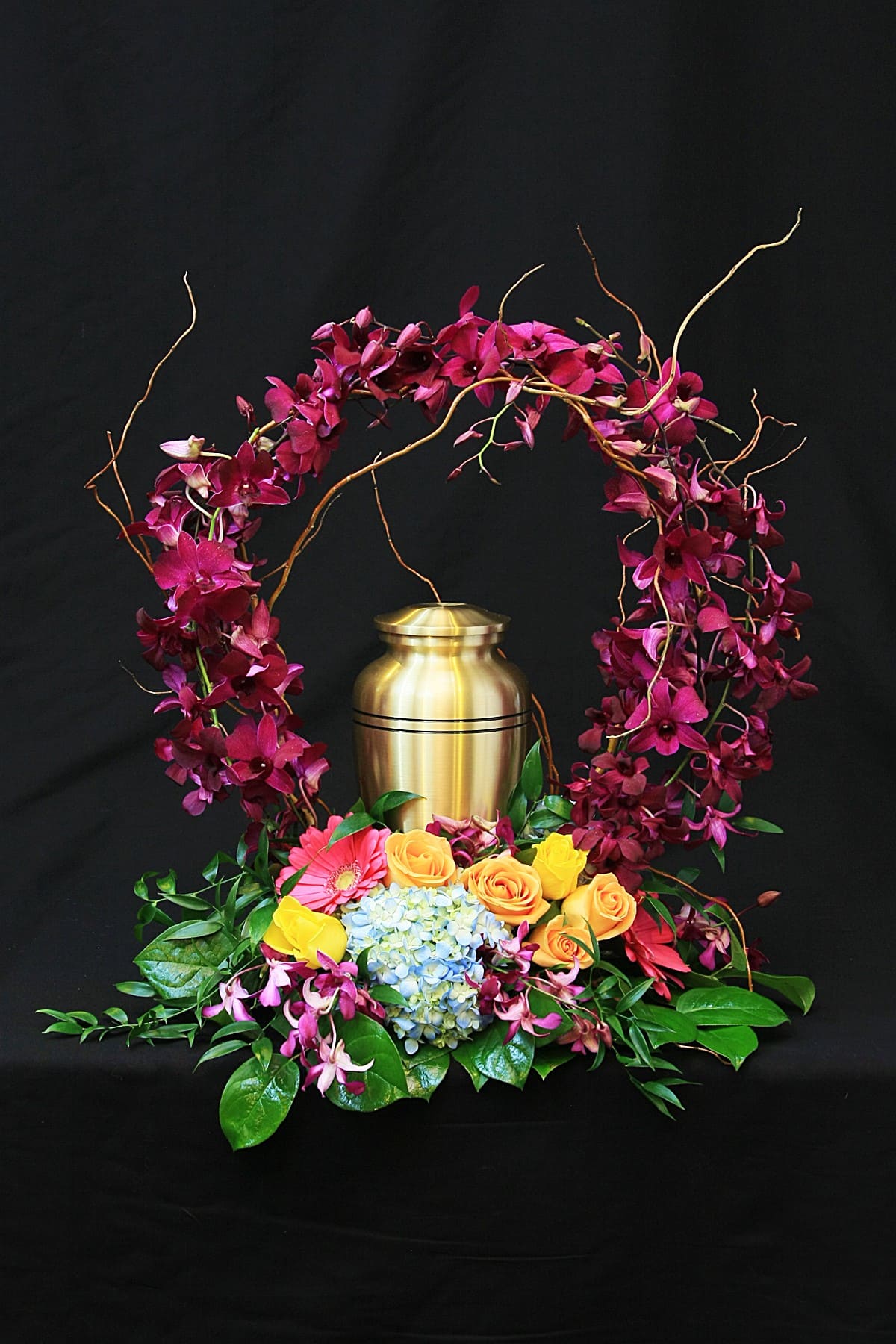 Floral urn arrangement with magenta orchids, roses, and hydrangea around a gold urn